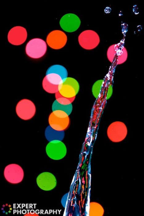 A water splash surrounded by colorful bokeh lights on black background